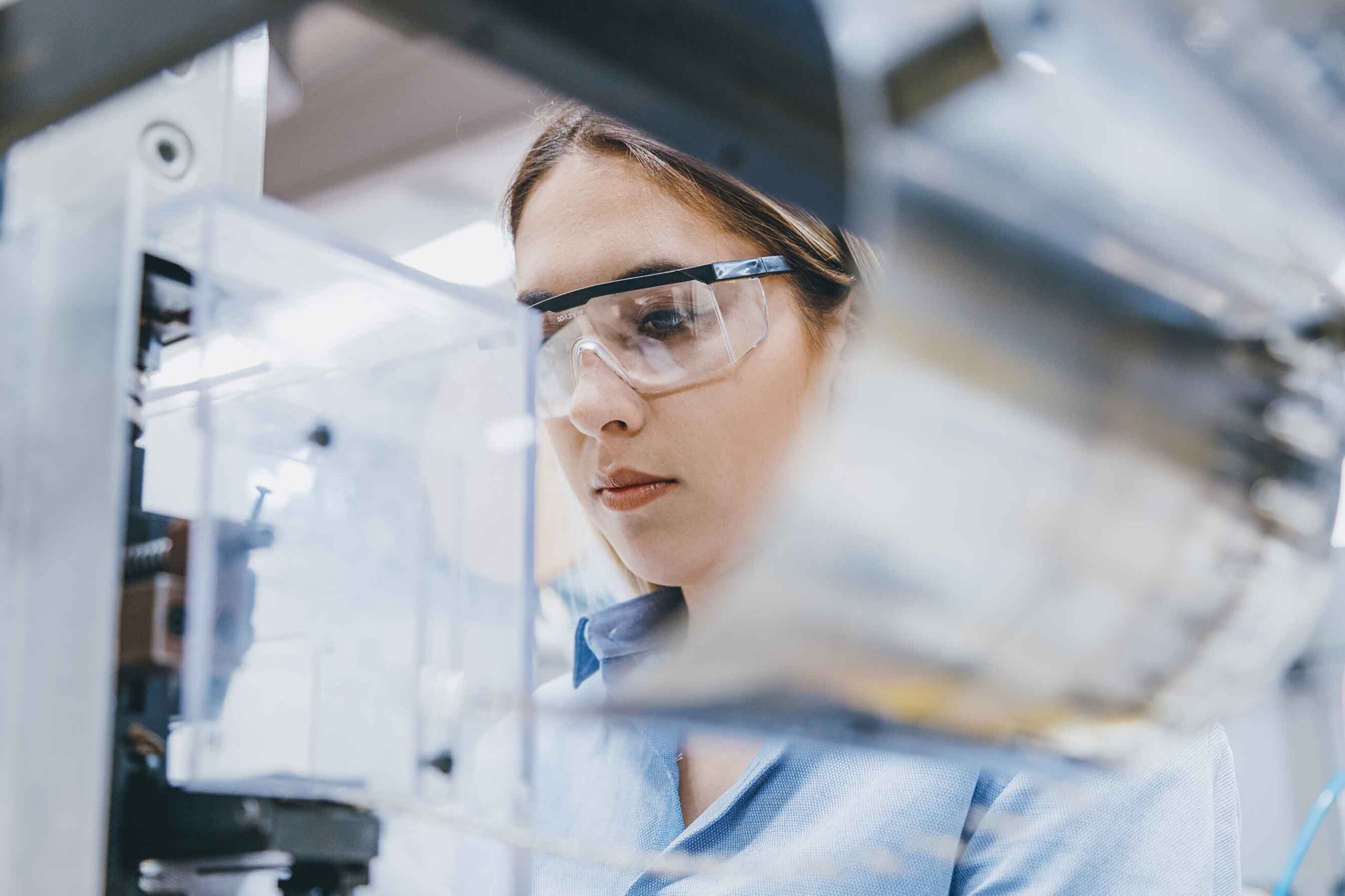 woman with protective glasses working in lab using a microscope